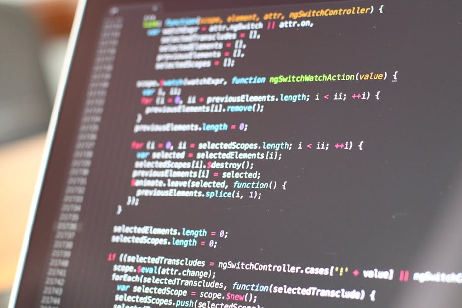 A computer monitor displaying a screen filled with lines of colorful, blurred programming code on a dark background. The code elements include various keywords, syntax, and symbols in red, green, blue