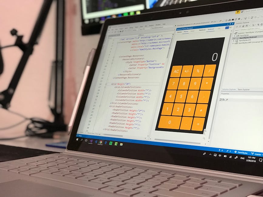 A person using a laptop computer with a dark-themed code editor or development environment displayed on the screen. The laptop is positioned on a dark surface, possibly a table or desk, with visible h
